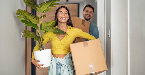 Jong stel is aan het verhuizen en hebben dozen en een plant in hun handen
