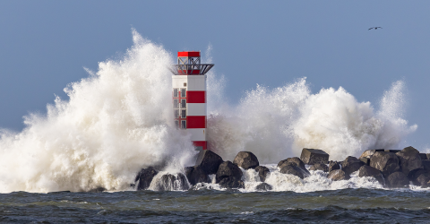 Door de harde wind ontstaan er hoge golven tegen een vuurtoren aan
